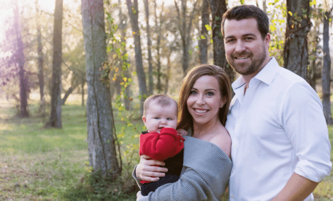 A man and woman hold a baby in a park, with Caroline from Swaddles and Bottles smiling beside them.