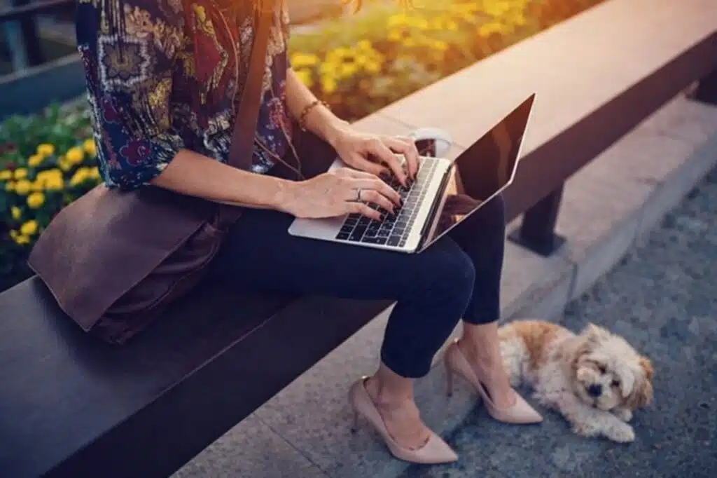 Female blogger working on laptop outdoors with dog, representing freelance blogging lifestyle