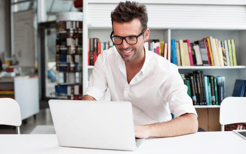 A man with glasses is diligently working on his laptop, showcasing concentration and productivity.