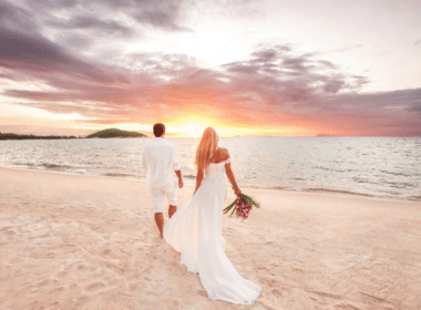 A bride and groom stroll hand in hand along the beach at sunset, showcasing a romantic beach wedding atmosphere.