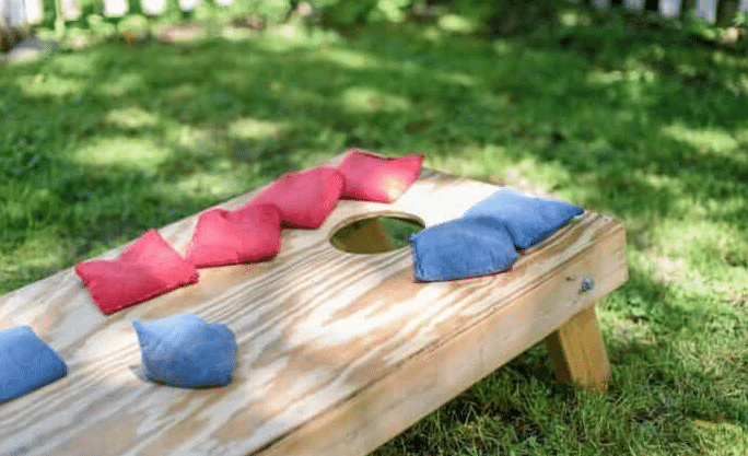A wooden cornhole game positioned in a yard, inviting participants to enjoy fun activities during a BBQ gathering.