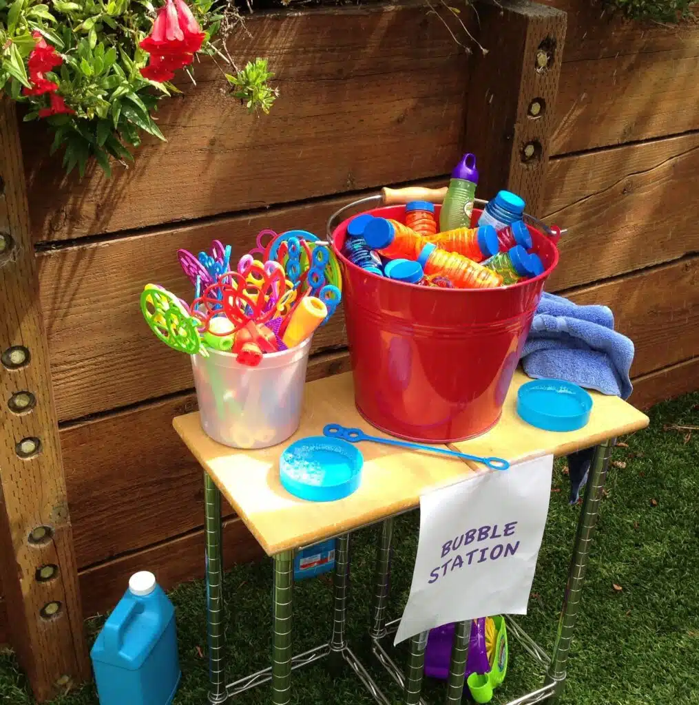 A table with a bucket of water and a sign stating "Balloon Magic" positioned on it.