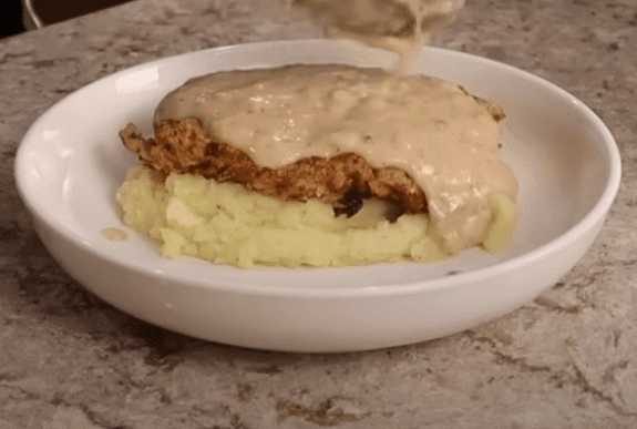 A person pours gravy over a serving of mashed potatoes, showcasing a delicious meal for two.