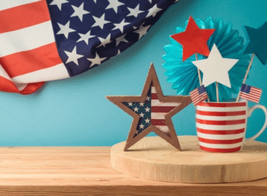 American flag and red, white, and blue decorations arranged on a wooden table for a DIY Fourth of July celebration.
