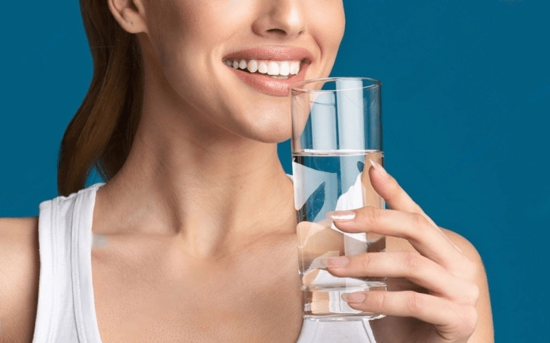 A woman smiling while holding a glass of water, promoting daily healthy habits for women.