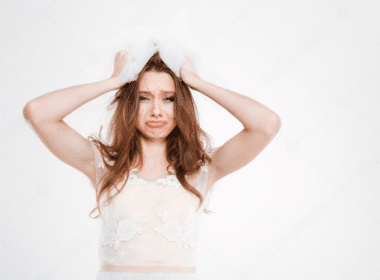 A woman in a wedding dress holding her head, reflecting on her wedding day amidst a backdrop of wedding planning materials.