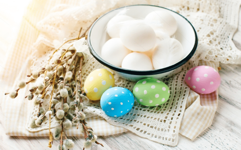 A bowl of colorful Easter eggs sits on a table next to a bowl of milk, showcasing a minimalist Easter theme.