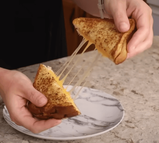 A person holds a golden-brown grilled cheese sandwich, showcasing its melted cheese and crispy exterior.