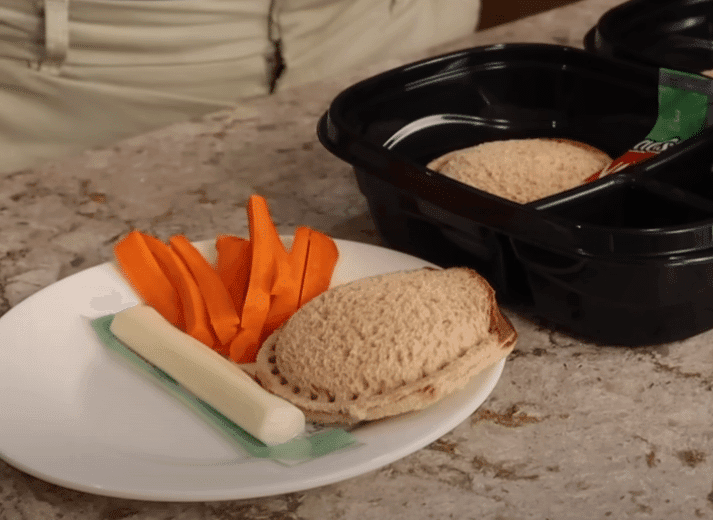 A plate featuring a sandwich, fresh carrots, and a slice of bread arranged neatly.