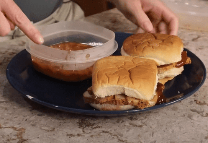 A person drizzles sauce onto a sandwich, preparing it for a meal.