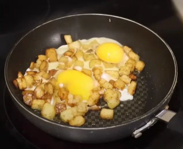 A frying pan filled with cooked potatoes and eggs, sizzling on a stovetop.