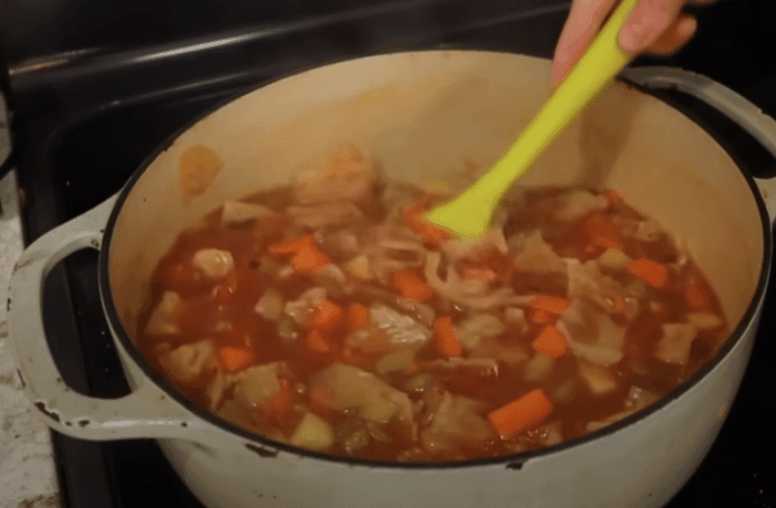 A person stirring a pot of vegetable soup with a spoon, focused on preparing a healthy meal.
