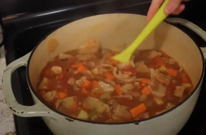 A person stirring a pot of vegetable soup with a spoon, focused on preparing a healthy meal.