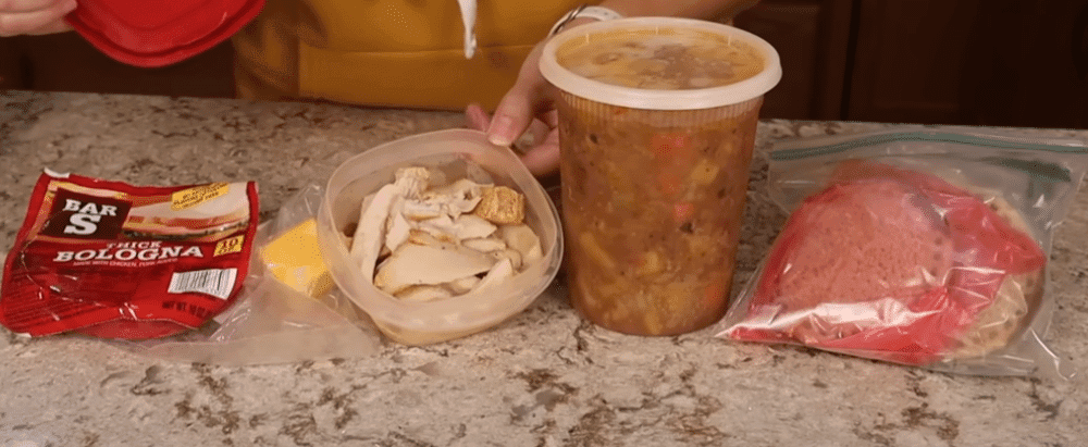 A woman holds a food container in one hand and a bag of meat in the other, preparing for a meal.