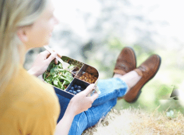 A woman sitting on the ground enjoying a plate of food, illustrating budget-friendly meal ideas.