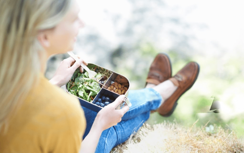 A woman sitting on the ground enjoying a plate of food, illustrating budget-friendly meal ideas.