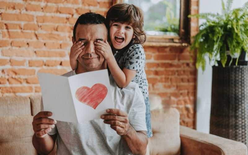 Father and son proudly hold a heart-shaped paper, showcasing a heartfelt DIY Father’s Day gift idea.