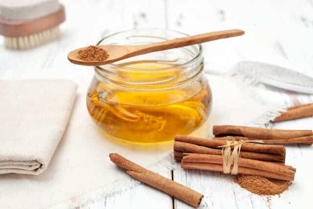 A jar of honey and cinnamon sits on a white wooden table, showcasing a natural remedy for skin treatment.