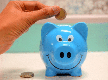 A person inserting a coin into a pink piggy bank, symbolizing saving money for future use.