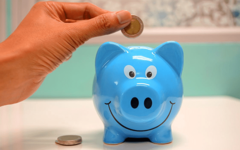 A person inserting a coin into a pink piggy bank, symbolizing saving money for future use.