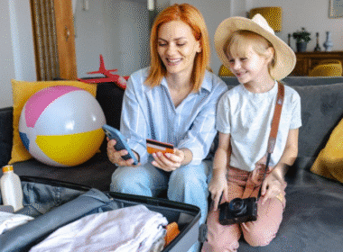 A woman and a child sit on a couch beside a suitcase, preparing for a Vacation Packing List Beach trip together.