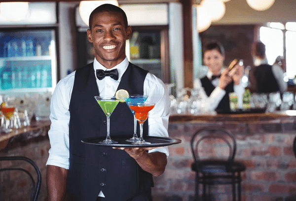 A bartender holds a tray with two colorful cocktails, ready to serve them to guests.