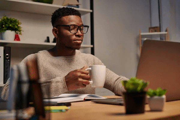 A man in glasses works at a desk with a laptop and coffee, promoting the idea of being a night owl online for pay.