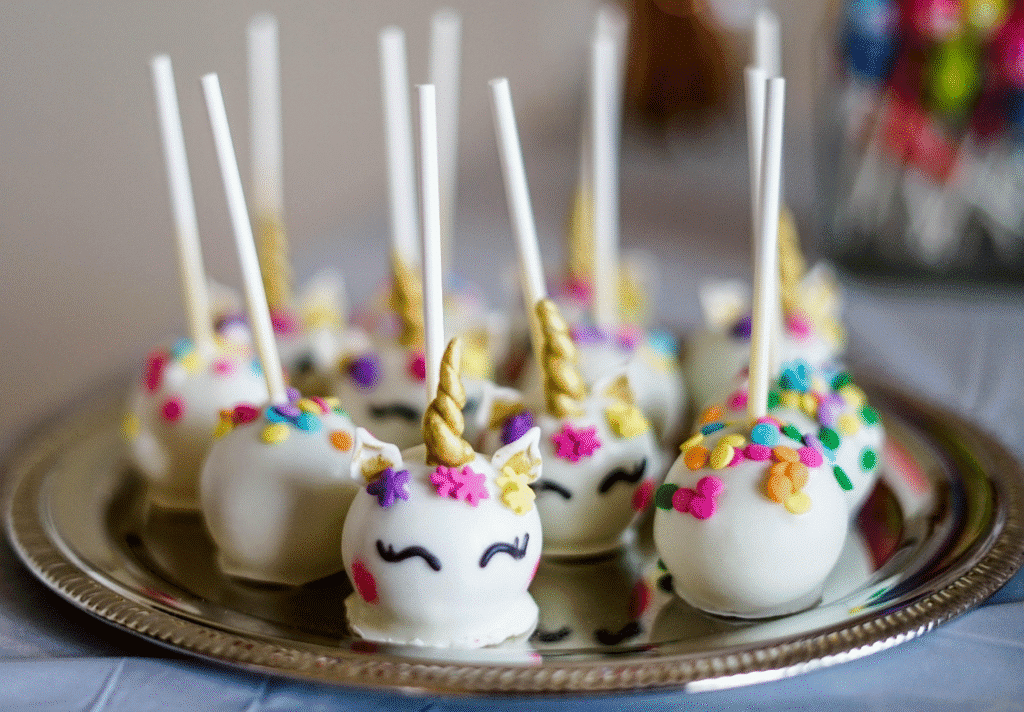 Colorful unicorn cake pops arranged on a silver platter, featuring whimsical designs and vibrant colors.