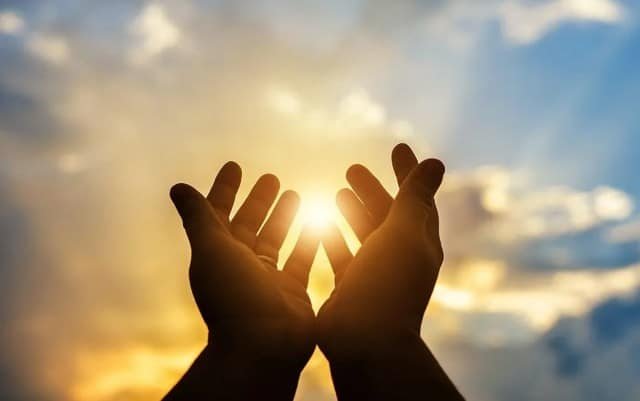 Hands reaching upward towards a bright sun against a clear blue sky, symbolizing hope and aspiration.