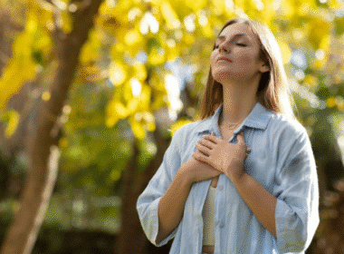 A woman stands before a tree, hands on her chest, reflecting on using prayer to seek employment opportunities.