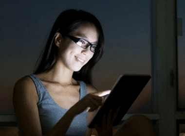 A woman wearing glasses uses a tablet computer at night, focused on her remote night job tasks.