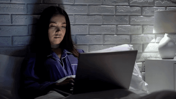 A woman comfortably seated in bed, working on her laptop for Scribie.