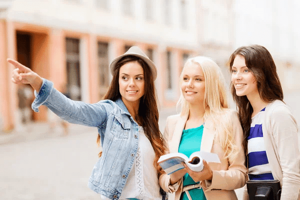 Three young women, acting as a tour guide, point to an interesting site on the street, engaging with their surroundings.
