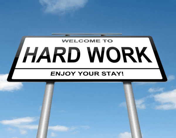 A welcoming sign that reads "Welcome to HARD WORK" with "ENJOY YOUR STAY!" below, set against a blue sky with clouds.