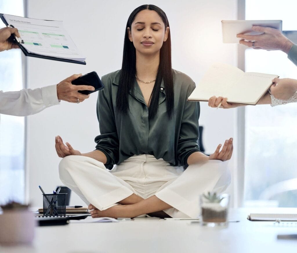 A woman meditates in an office surrounded by colleagues, embodying the theme "You're Not Lazy, You're Just Quiet."