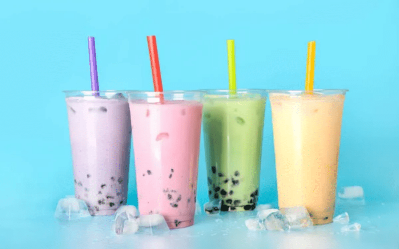 Four colorful bubble tea drinks in glasses on a blue background, showcasing vibrant flavors for a food marketing concept.