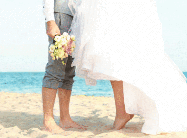 A bride and groom stand together on a beach, celebrating their wedding in a picturesque destination setting.