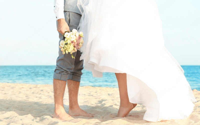 A bride and groom stand together on a beach, celebrating their wedding in a picturesque destination setting.