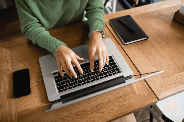 A woman focused on data entry, typing on a laptop at a table in a well-lit workspace.