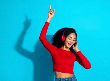 A woman in a red shirt and headphones dances joyfully, promoting the idea of getting paid to listen to music.