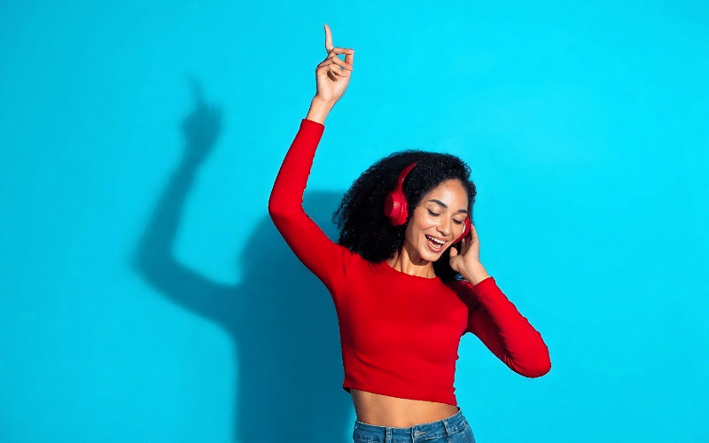 A woman in a red shirt and headphones dances joyfully, promoting the idea of getting paid to listen to music.