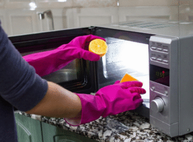 A person in gloves cleans a microwave with a DIY stainless steel cleaner, focusing on removing stains and smudges.