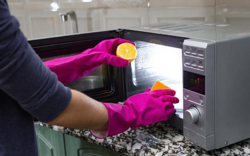 A person in gloves cleans a microwave with a DIY stainless steel cleaner, focusing on removing stains and smudges.