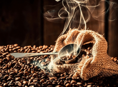 A close-up of coffee beans scattered next to a silver spoon, suggesting a natural car freshener idea.