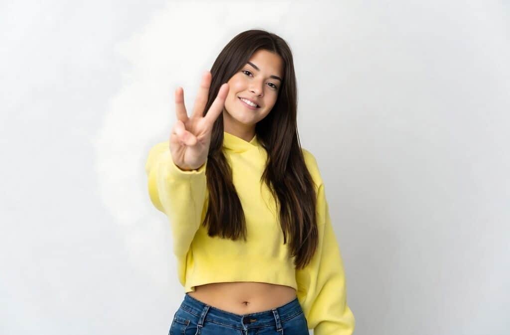 A young woman wearing a yellow shirt and jeans gives a peace sign, exemplifying the three-color rule in fashion.