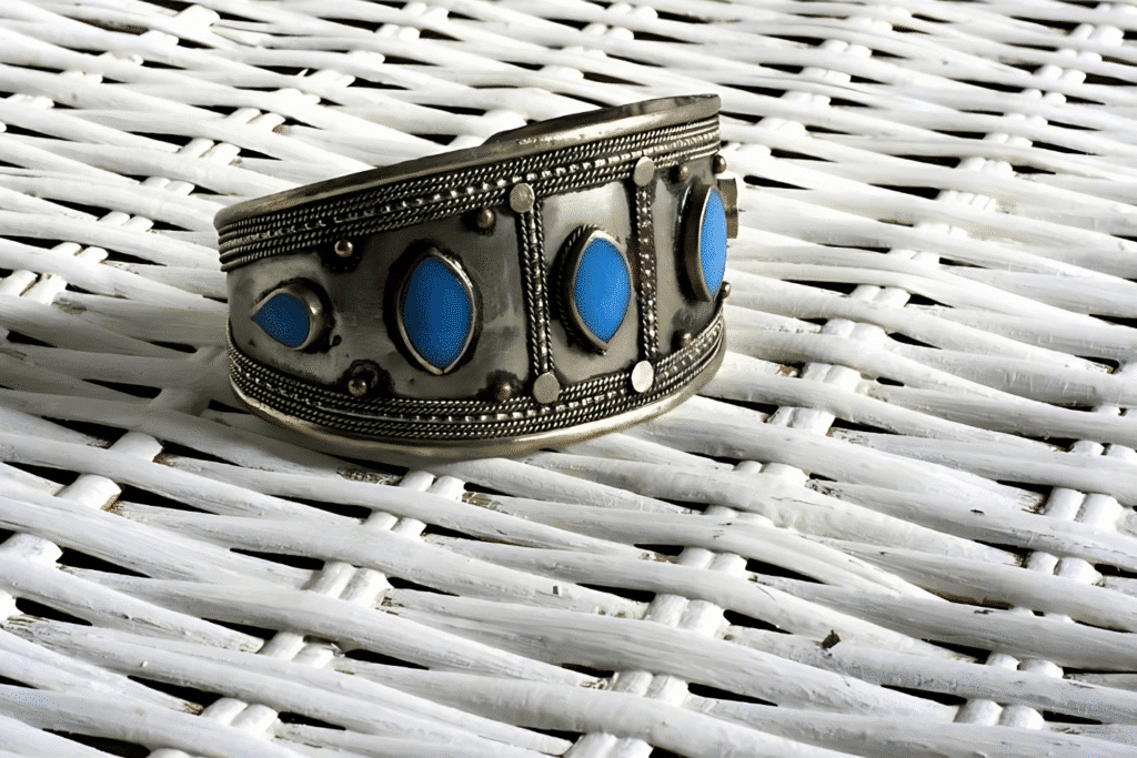 A silver cuff adorned with blue stones rests on a wicker basket, showcasing elegant costume jewelry.