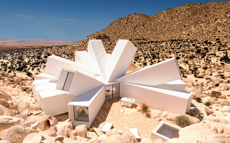 A white house in the desert surrounded by rocks, showcasing a DIY shipping container home in a rugged landscape.
