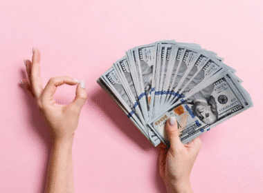 A person holding a stack of cash against a pink background, illustrating financial themes for Pinterest pin creation.
