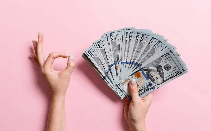 A person holding a stack of cash against a pink background, illustrating financial themes for Pinterest pin creation.
