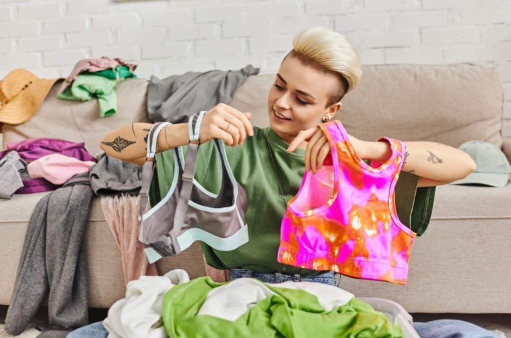 A woman sits on a couch surrounded by clothes on the floor, illustrating tips for selling and showcasing clothing effectively.
